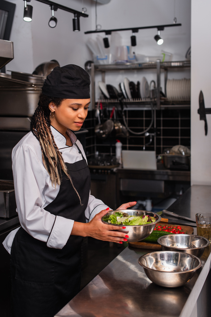 молодий афроамериканський шеф-кухар тримає миску з салатом на професійній кухні
 - Фото, зображення