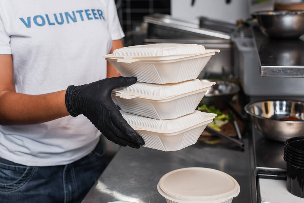 cropped view of young african american social worker holding plastic containers in kitchen - Foto, Imagem