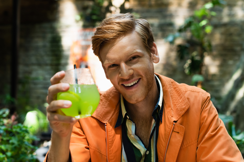happy redhead man holding glass with cocktail in outdoor terrace of bar - Foto, Bild