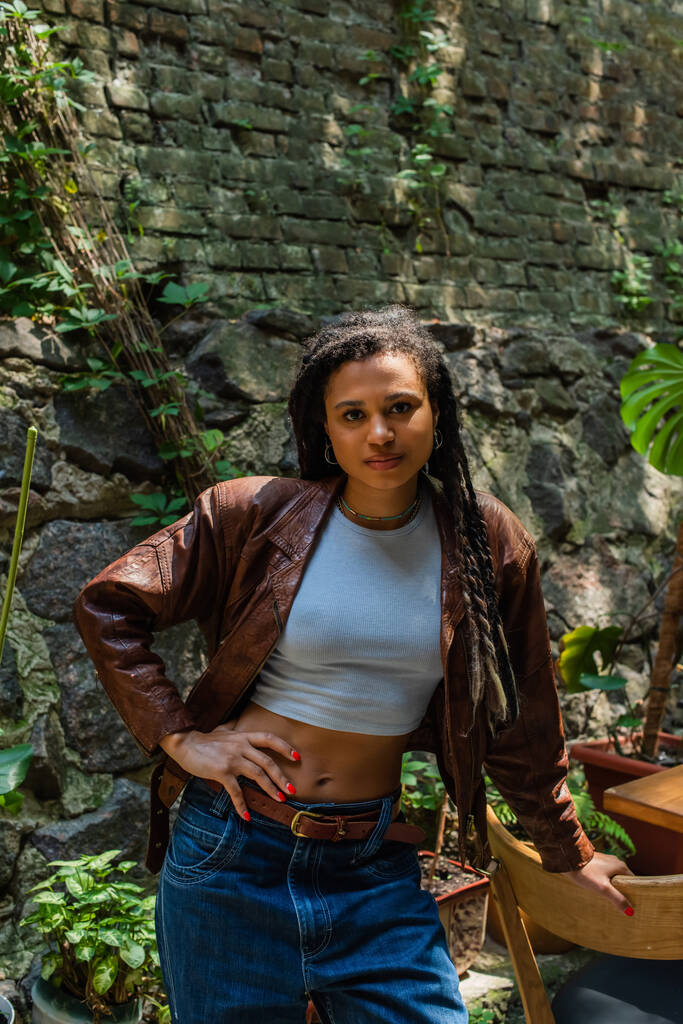 young african american woman in brown leather jacket standing with hand on hip  - Fotografie, Obrázek