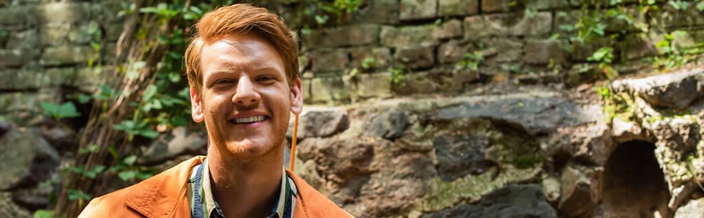 cheerful redhead man in orange jacket smiling outside, banner - 写真・画像