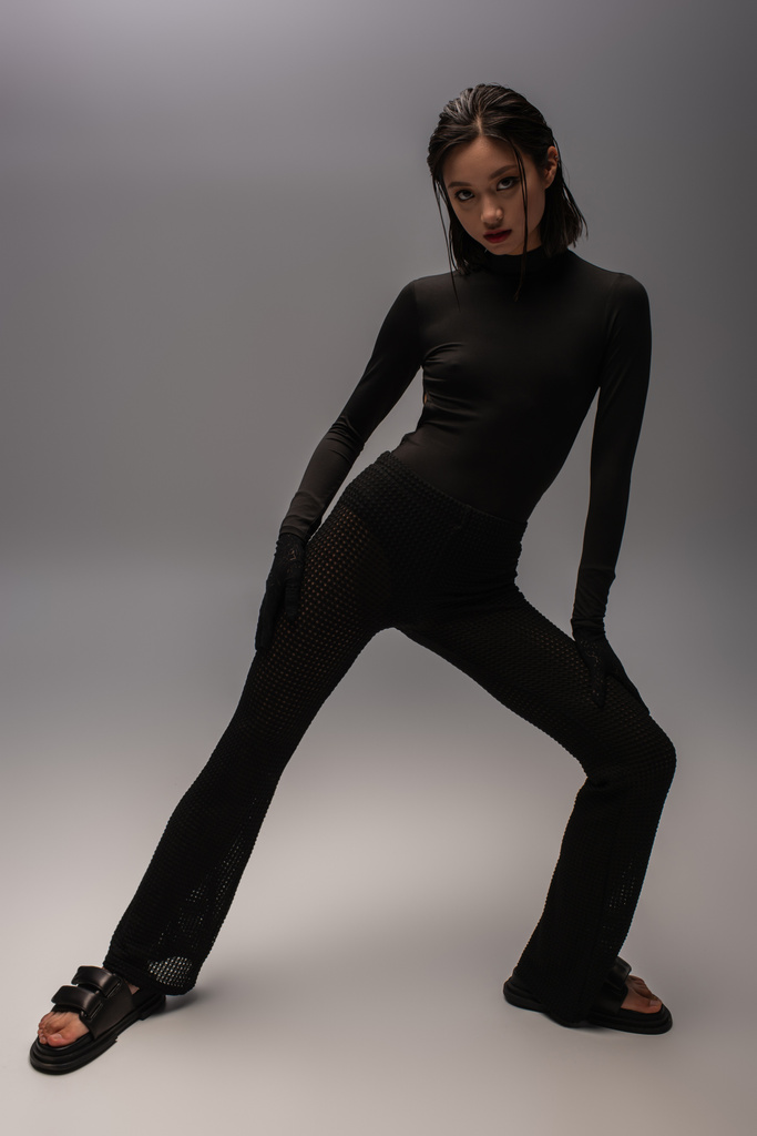 full length of young asian woman in total black outfit posing on grey  - Foto, immagini