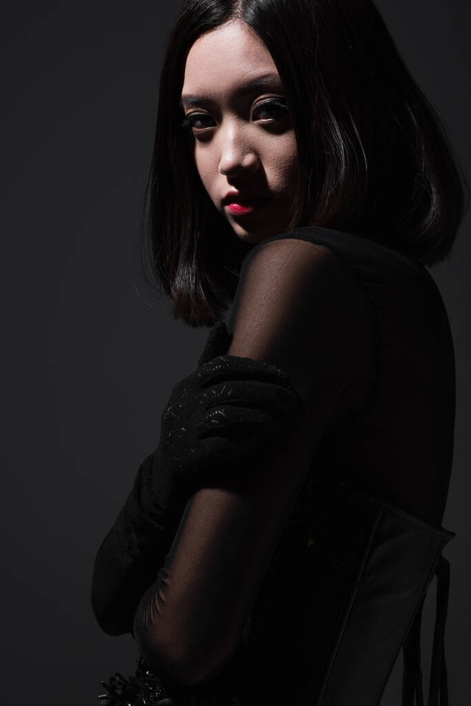 portrait of sensual asian woman in gothic black outfit looking at camera isolated on grey - Photo, image