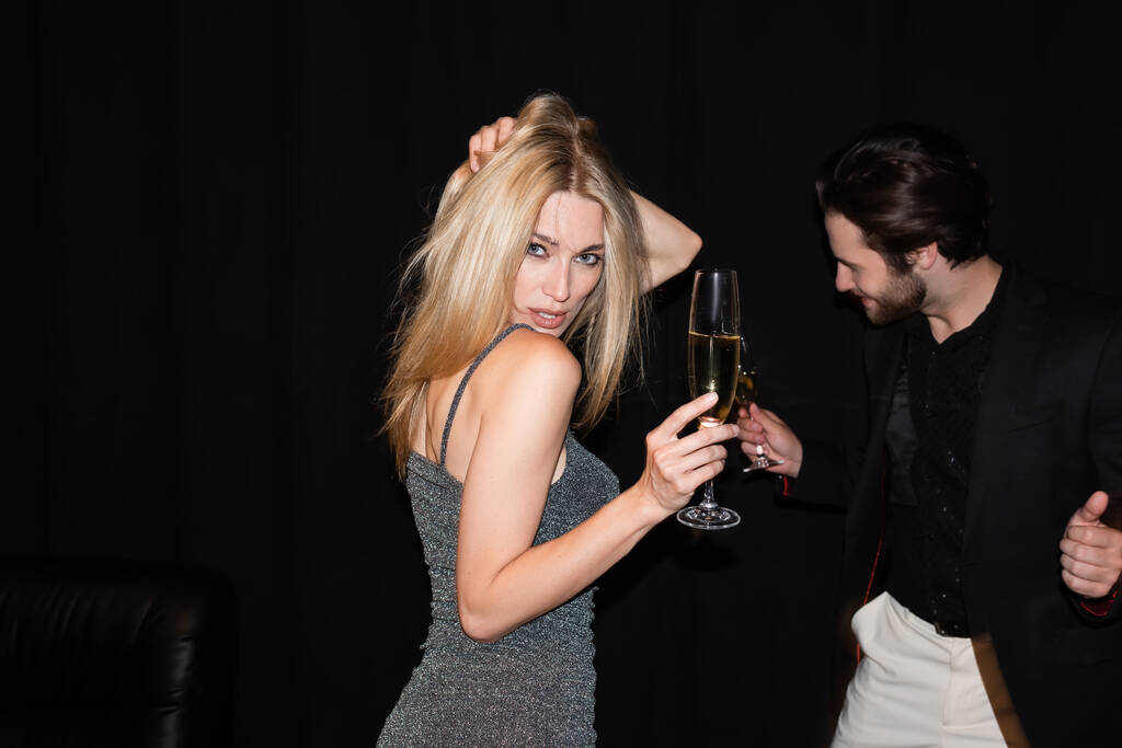 Сексуальна жінка в одязі тримає шампанське під час танців біля хлопця ізольовано на чорному
  - Фото, зображення