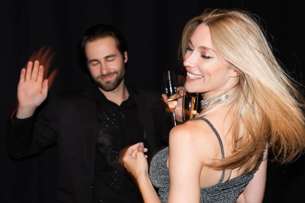 Motion blur of smiling woman with champagne dancing with boyfriend isolated on black  - Valokuva, kuva