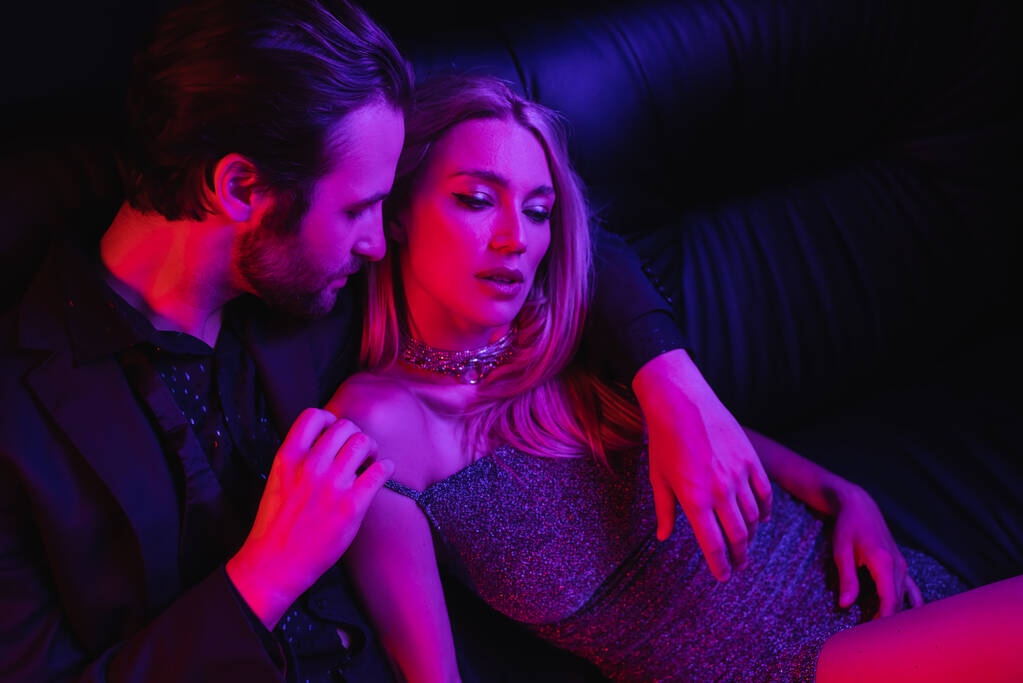Сексуальний чоловік роздягається білява дівчина в одязі на шкіряному дивані з освітленням ізольовано на чорному
  - Фото, зображення