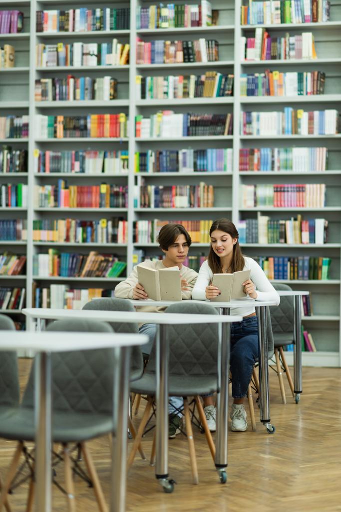 teenage students reading books near bookshelves in library - Fotó, kép