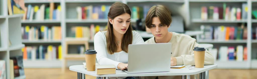 teenage friends looking at laptop while studying in library reading room, banner - Foto, Imagen