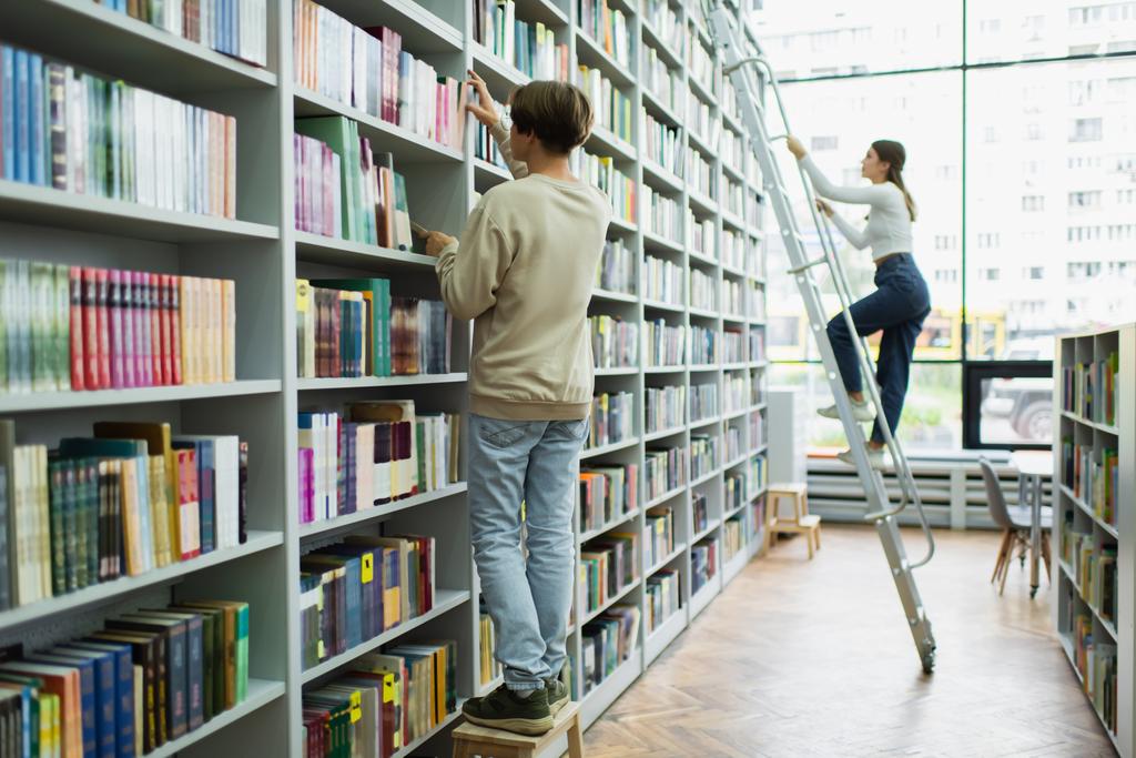 full length of teenage students choosing books on racks in library - 写真・画像