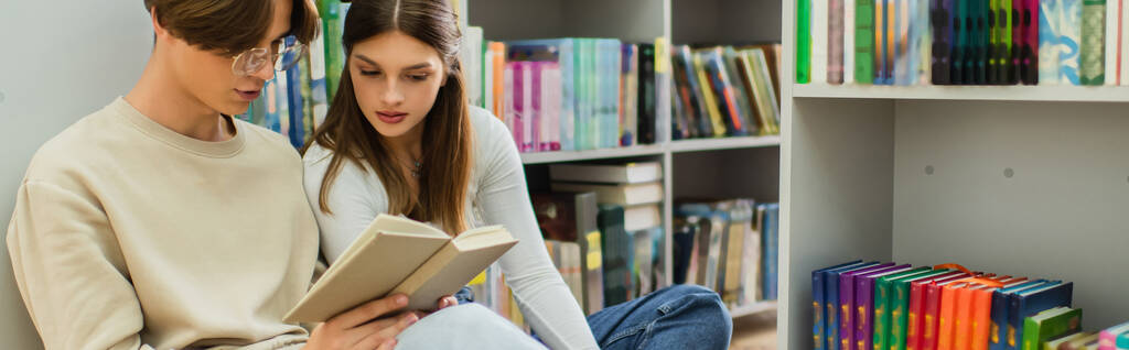 couple of students reading book while sitting near shelves in library, banner - Foto, Imagem
