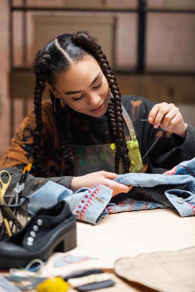 Young african american craftswoman embroidering denim jacket in workshop  - Fotografie, Obrázek