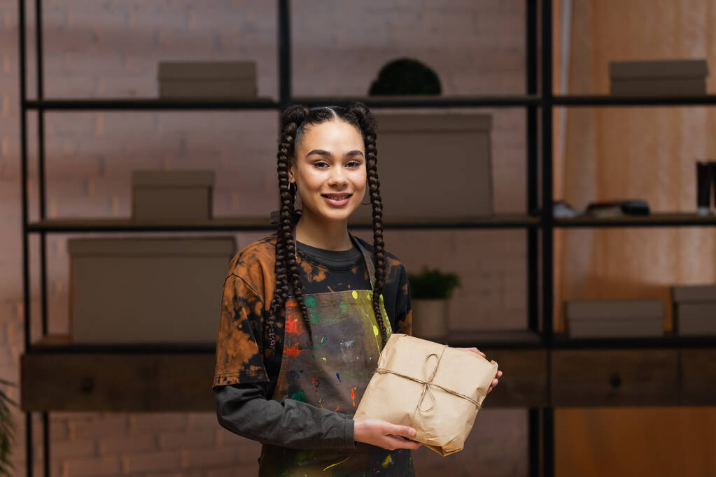 Улыбающаяся африканская американская ремесленница держит пакет в мастерской  - Фото, изображение