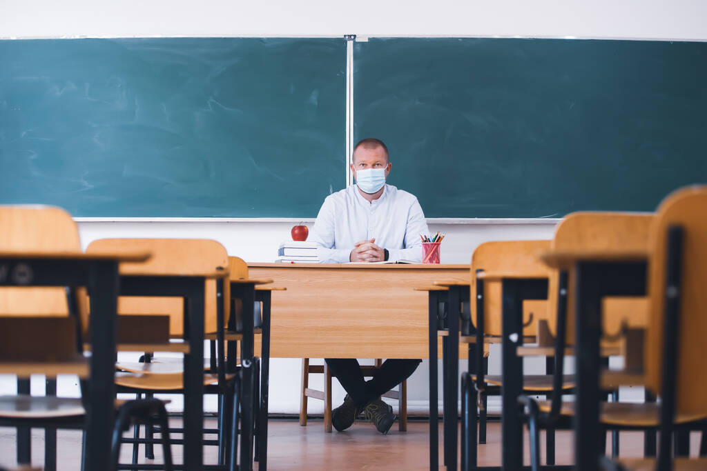 Учитель в маске в классе. Социальное разделение и безопасность в классе во время эпидемии коронавируса - Фото, изображение