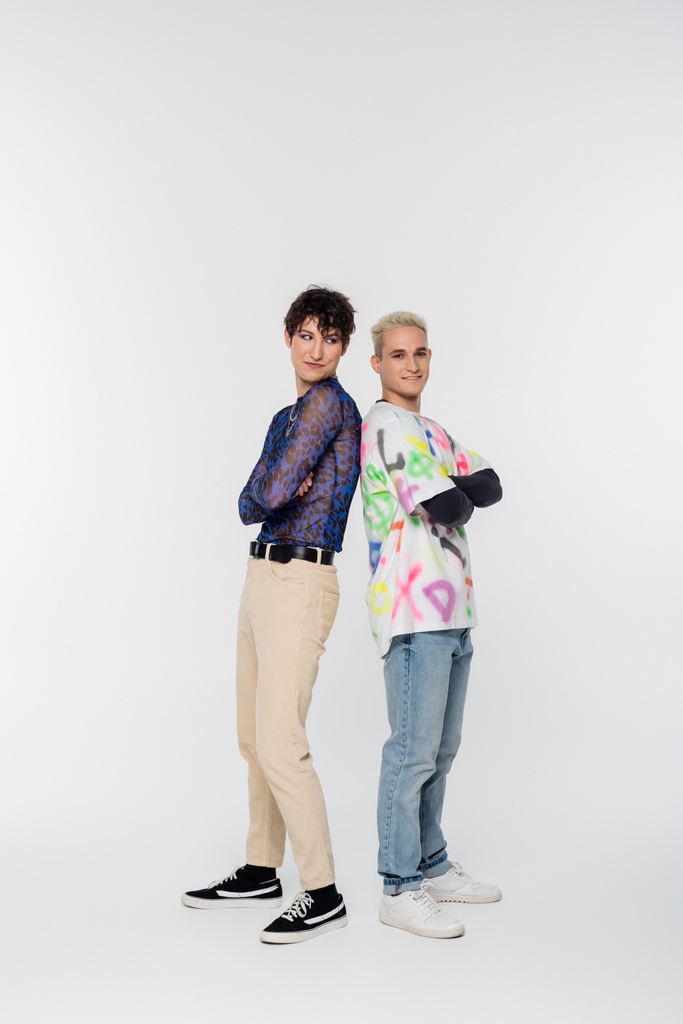full length of trendy gay man and queer person standing back to back with crossed arms on grey background - 写真・画像