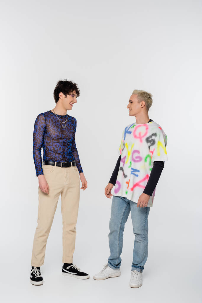 full length of happy gay man and queer person looking at each other on grey background - Foto, afbeelding