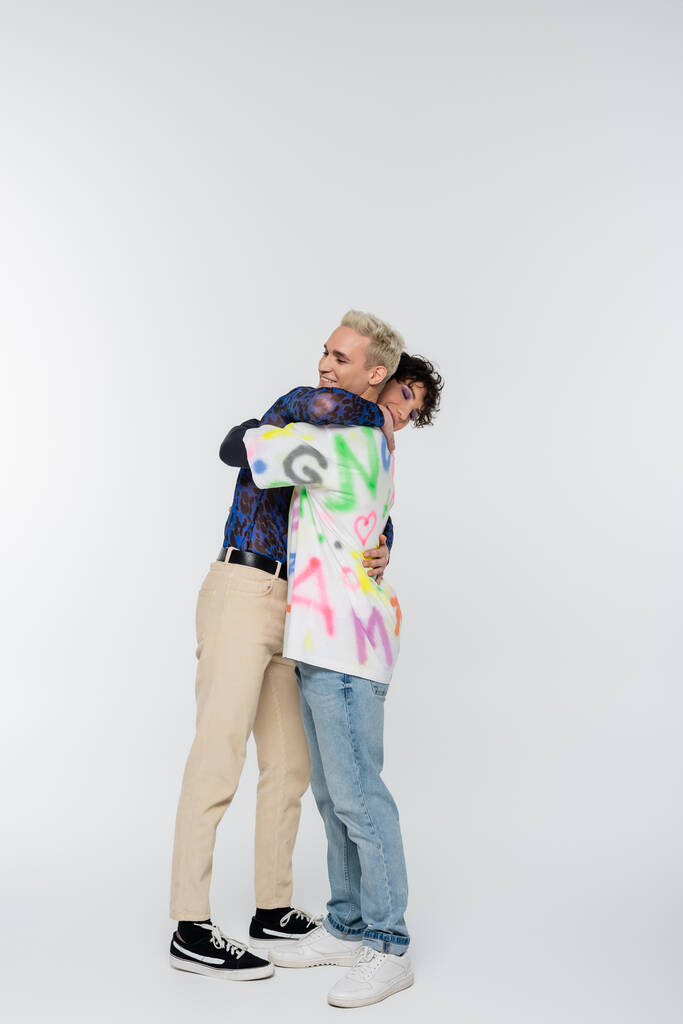 side view of young and stylish gay and queer person embracing on grey background - Foto, imagen