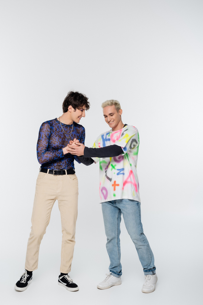 full length of positive gay holding hands of stylish queer person on grey background - Foto, Imagem