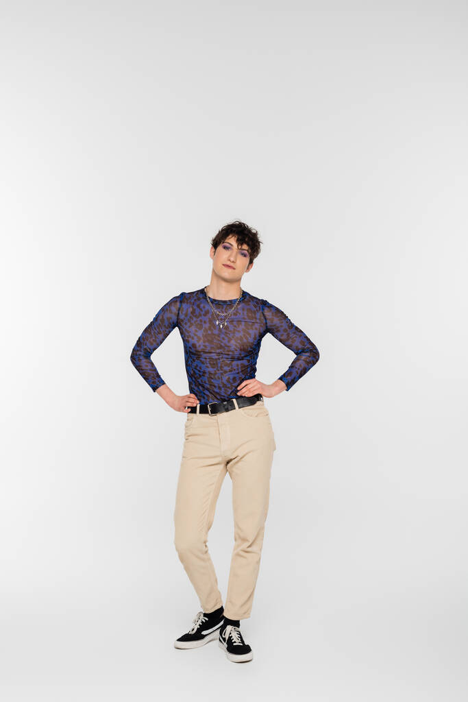 full length of nonbinary model in beige trousers posing with hands on waist on grey background - Foto, immagini