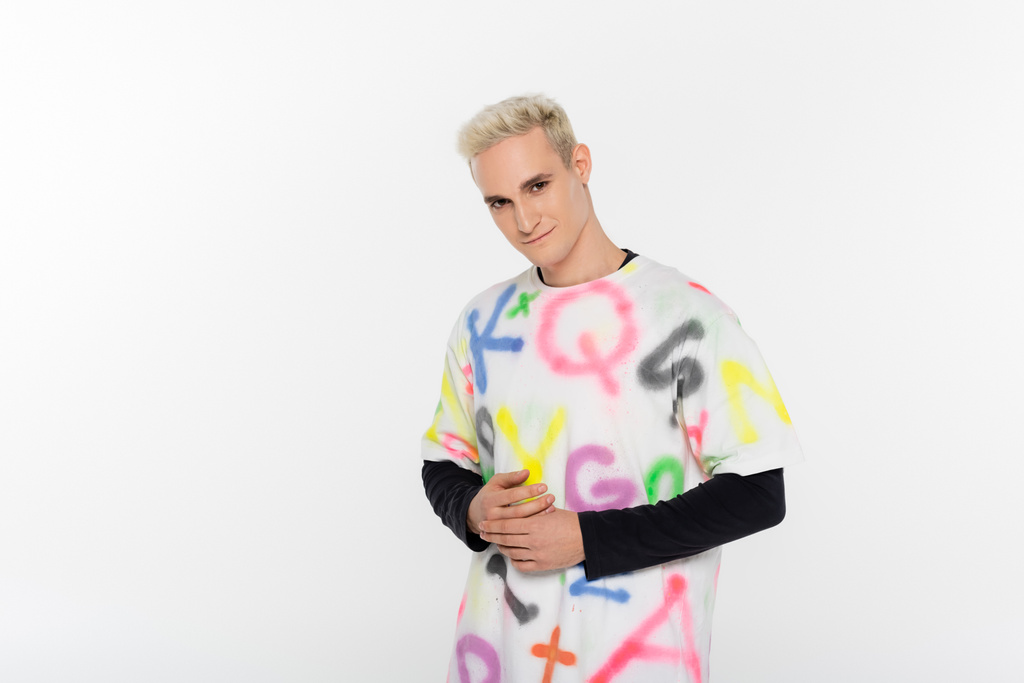 blonde gay man in fashionable t-shirt smiling at camera isolated on grey - Fotoğraf, Görsel