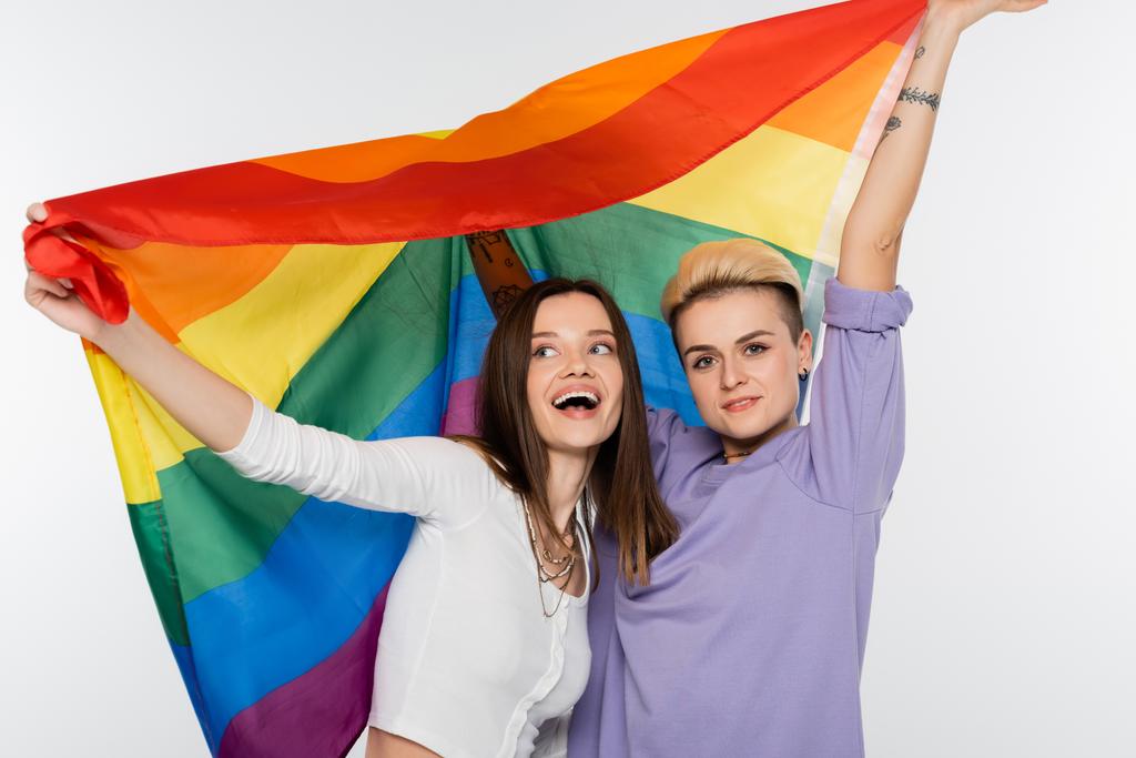 cheerful young lesbians holding lgbtq flag isolated on grey - Foto, imagen