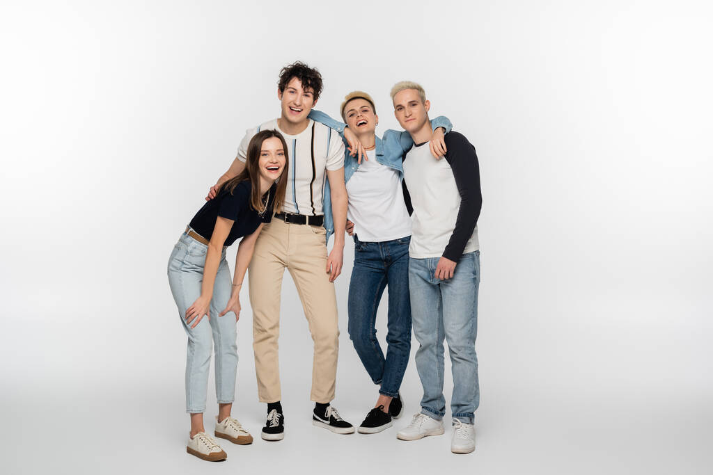 full length of young and stylish friends laughing on grey background - Foto, Bild