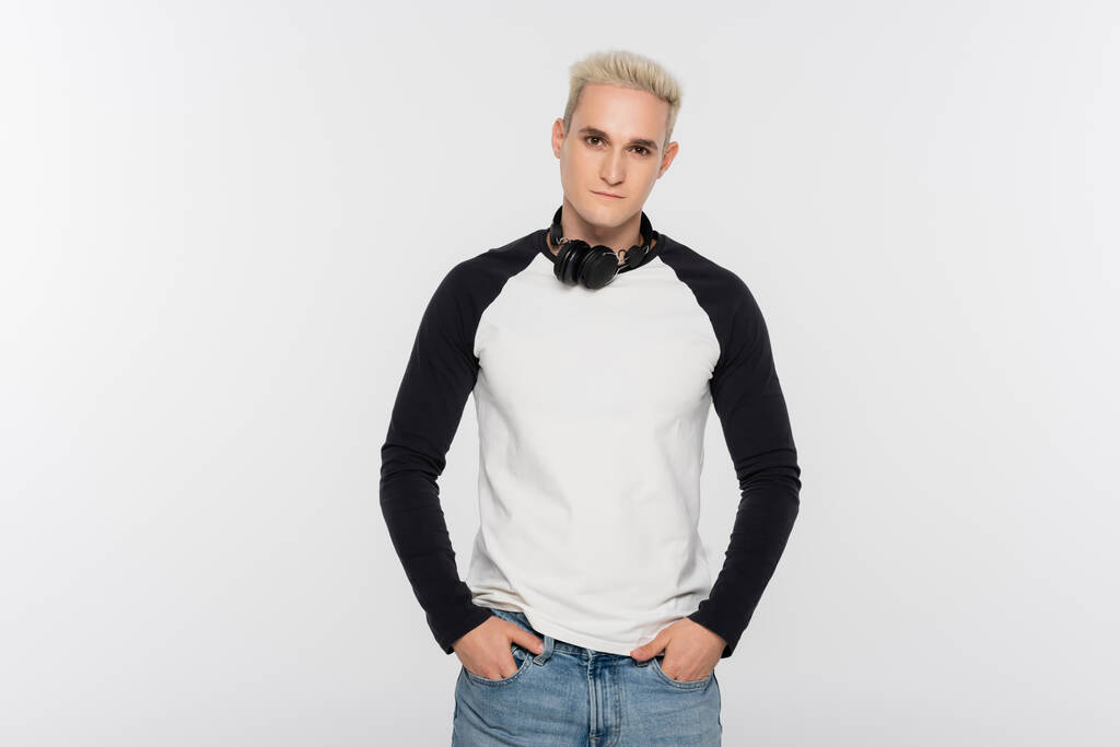 blonde man with headphones holding hands in pockets of jeans isolated on grey - Zdjęcie, obraz