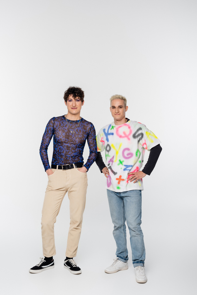 full length of positive gay man and queer person in stylish clothes posing on grey background - Foto, Bild