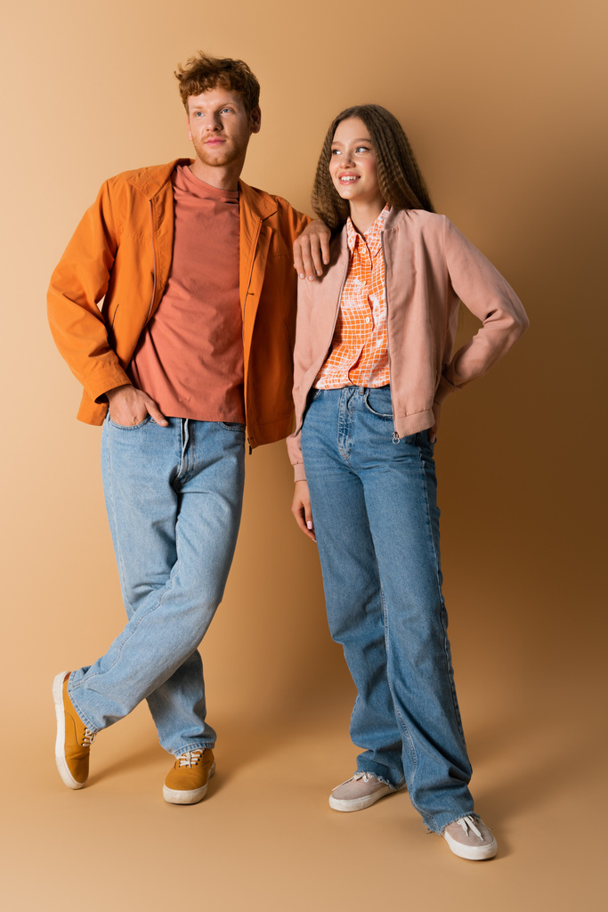 full length of cheerful and young couple in denim jeans standing on beige - Foto, Bild