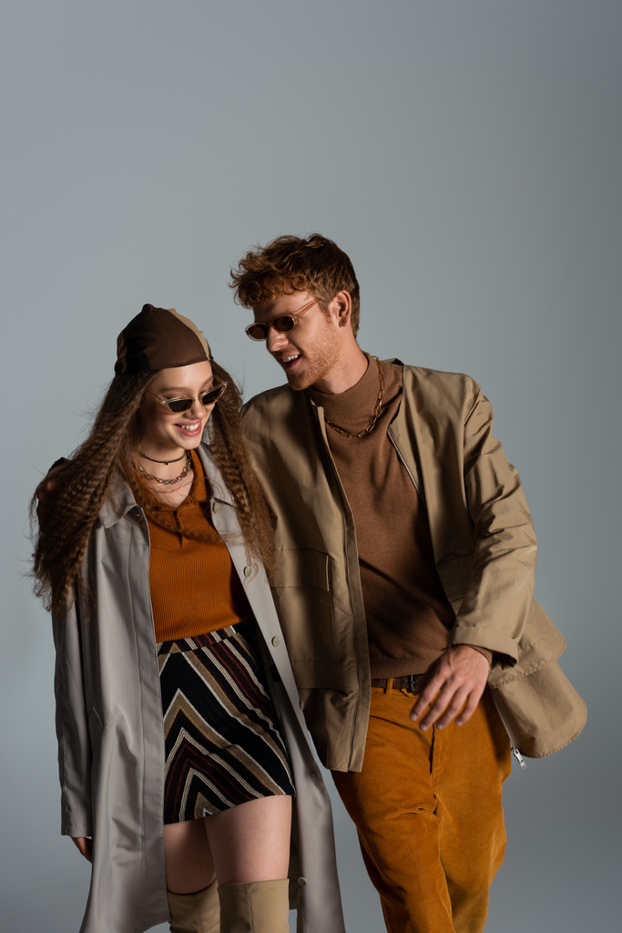 happy young couple in autumnal outfits and sunglasses smiling isolated on grey - 写真・画像