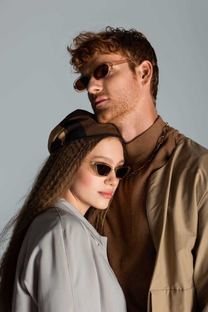young couple in sunglasses and autumnal clothes standing together isolated on grey - Foto, Imagem