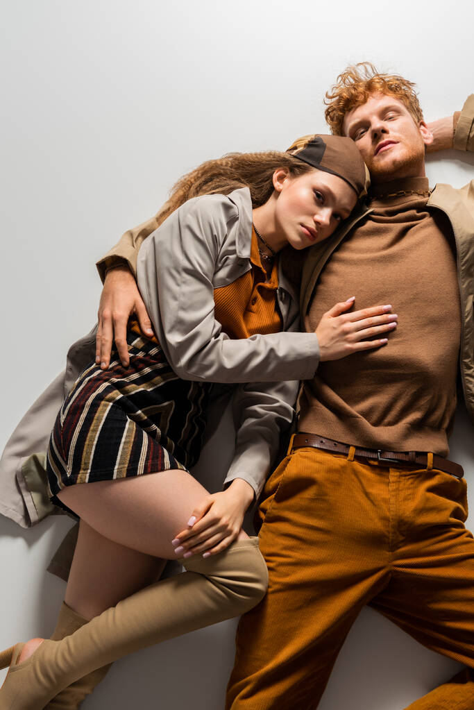 top view of stylish young man and girl in autumnal outfits lying together on grey  - 写真・画像