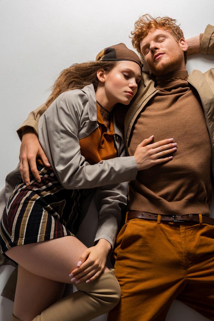 top view of stylish young couple with closed eyes lying in autumnal outfits on grey  - Foto, Bild