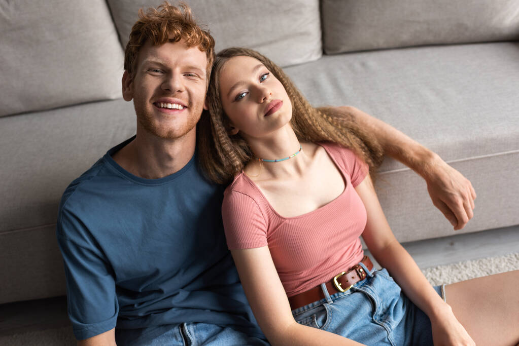 high angle view of young couple smiling while sitting near couch in modern living room - Φωτογραφία, εικόνα