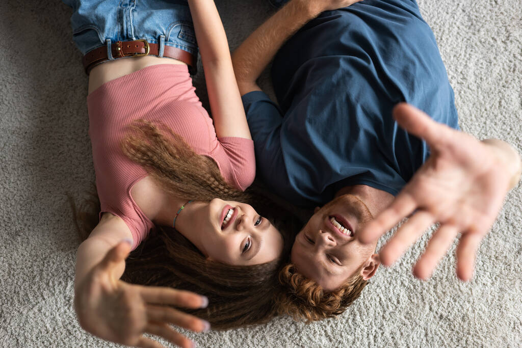 вид зверху щасливий і молодий чоловік і весела дівчина жестикулює, лежачи на килимі
  - Фото, зображення