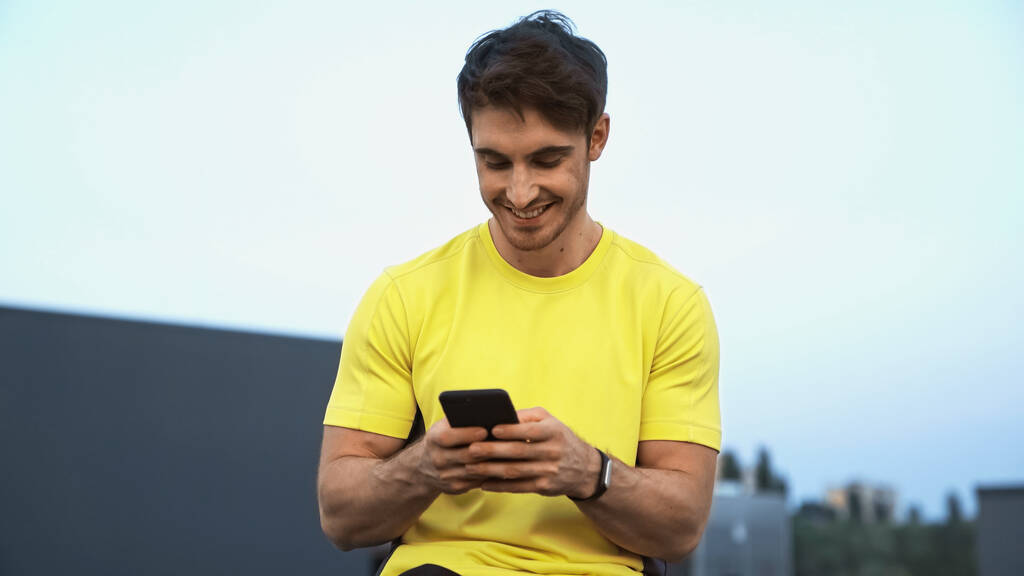 Щасливий молодий спортсмен, використовуючи мобільний телефон на даху ввечері
  - Фото, зображення