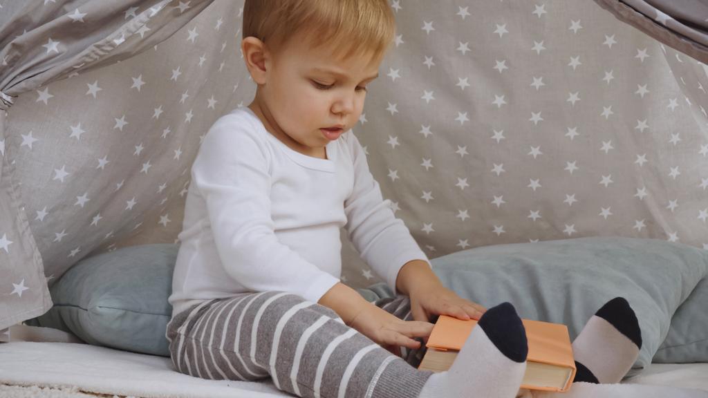 curious toddler boy sitting in baby wigwam and holding book - Zdjęcie, obraz