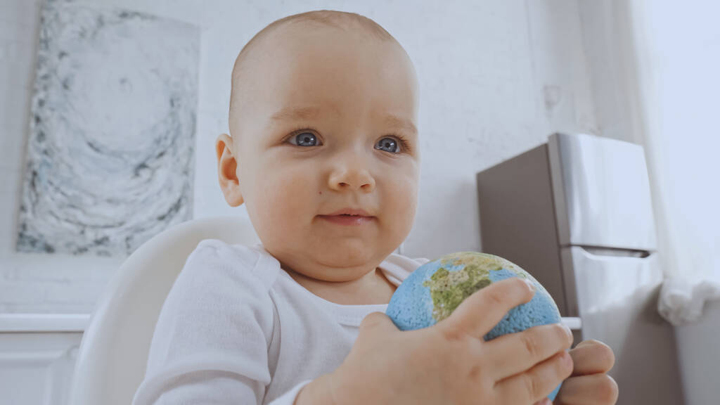 baby girl with blue eyes sitting on chair and holding small globe - Foto, afbeelding