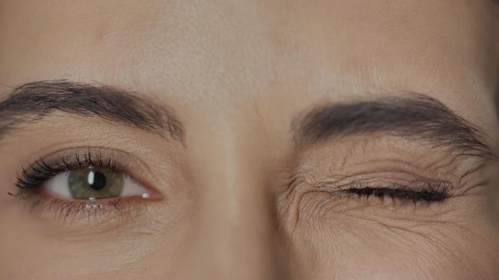 close up view of woman with hazel eyes and mascara on eyelashes winking while looking at camera  - Foto, Bild