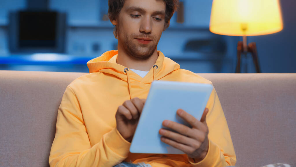 young man in yellow hoodie using digital tablet in living room  - Foto, Imagen