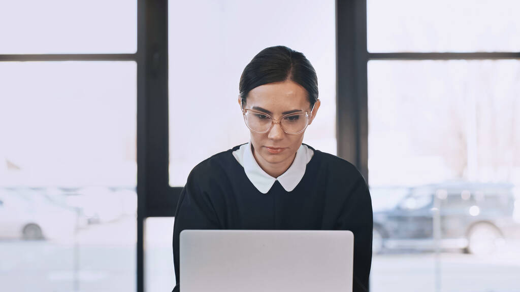 focused businesswoman in eyeglasses working on laptop in office - Photo, image