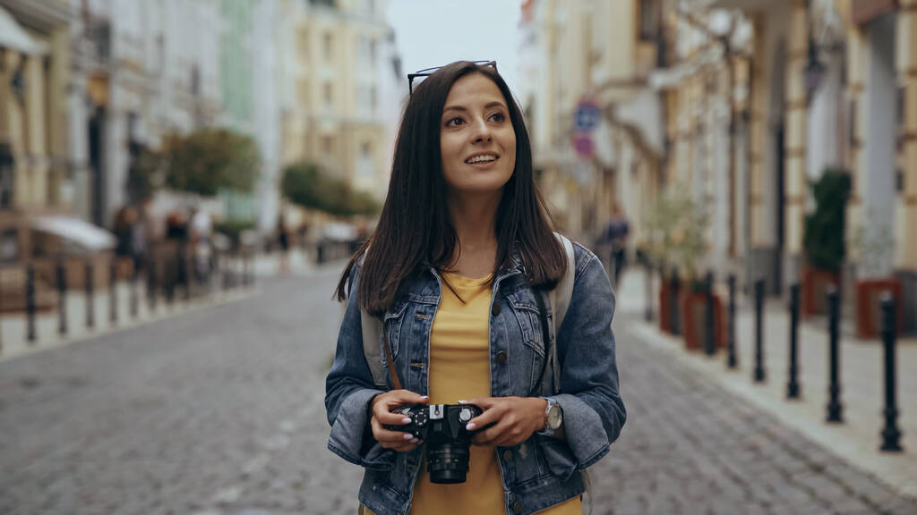 Cheerful tourist holding vintage camera on urban street  - Photo, Image