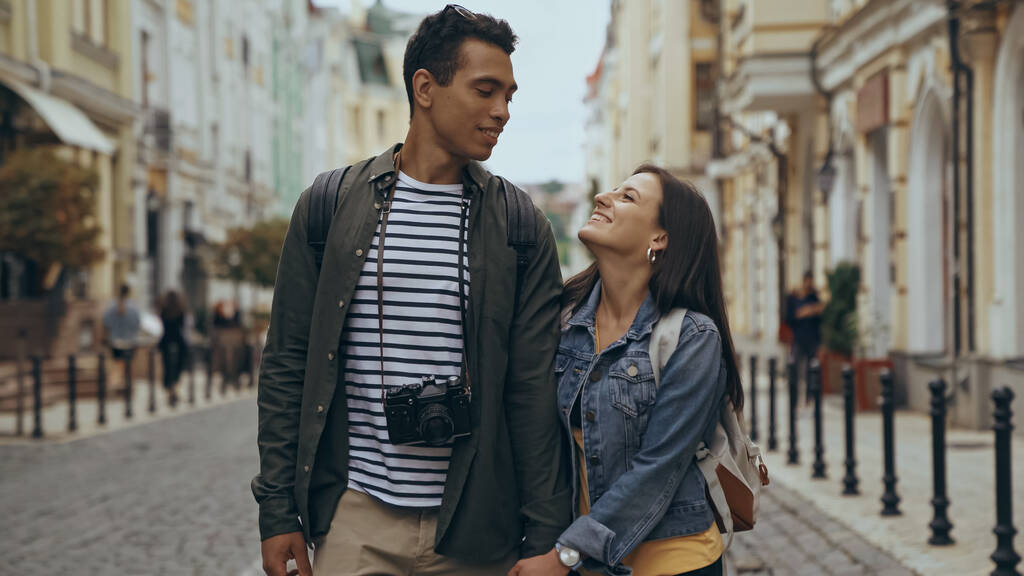 Cheerful interracial travelers looking at each other on urban street  - Foto, Bild