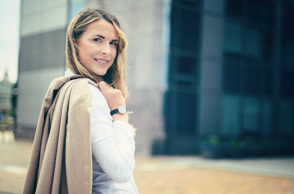 Confiante jovem gerente do sexo feminino segurando seu casaco ao ar livre em um cenário urbano moderno - Foto, Imagem