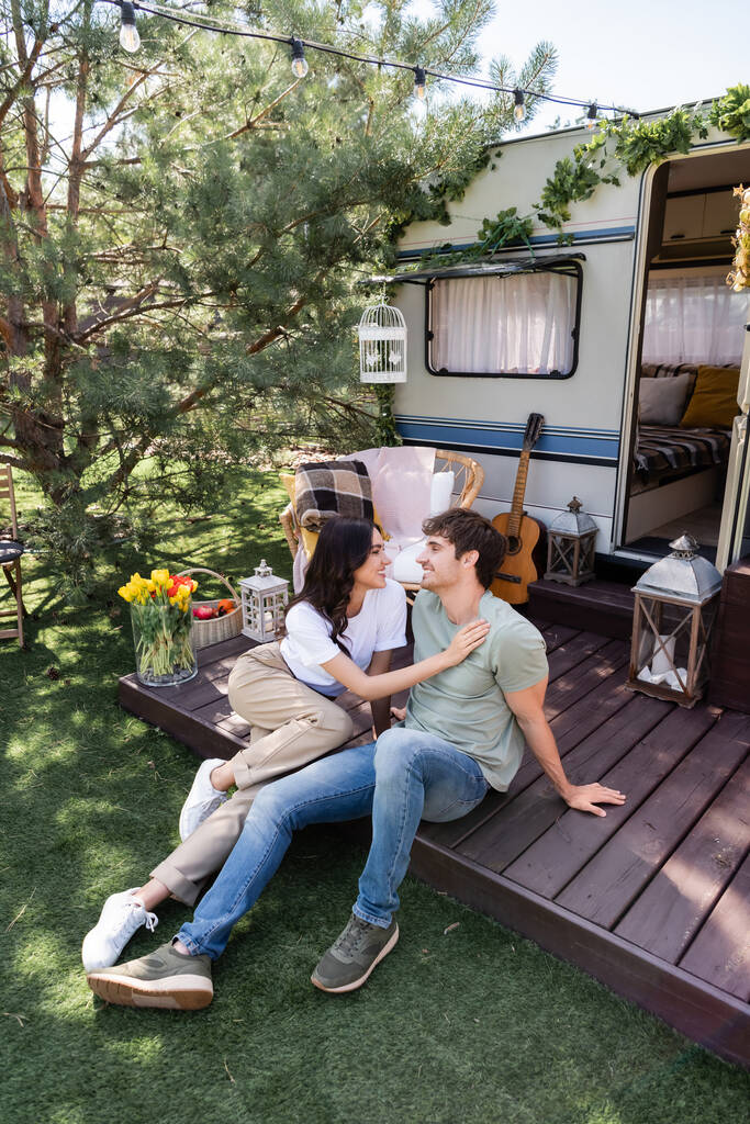 Side view of smiling woman touching boyfriend on terrace of camper van  - Фото, изображение