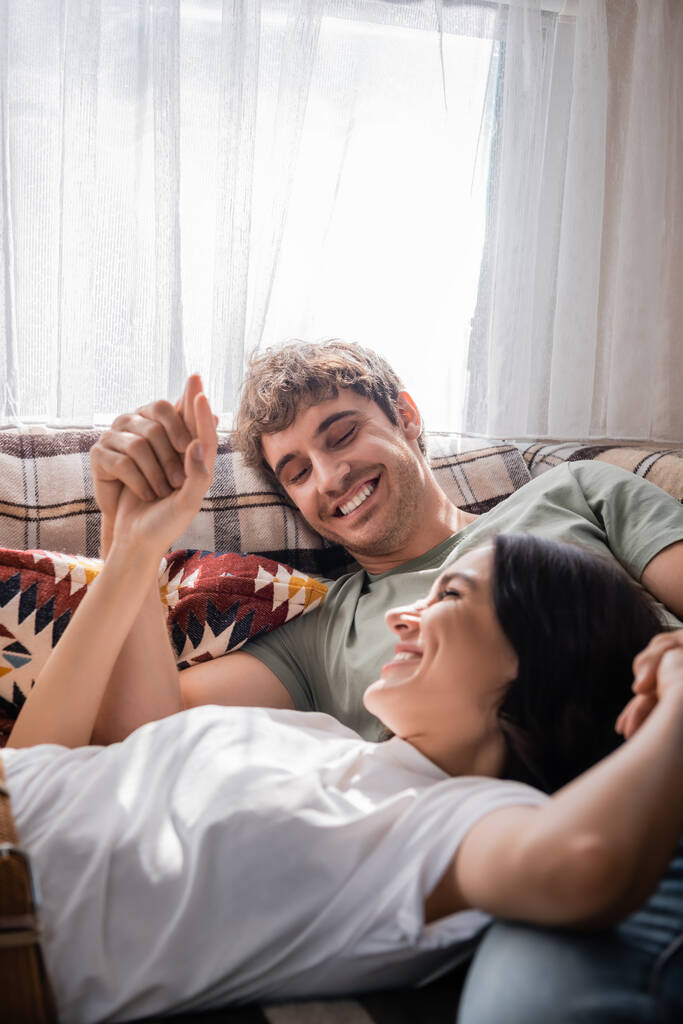 Positive couple holding hands while lying on bed in camper van  - Photo, image