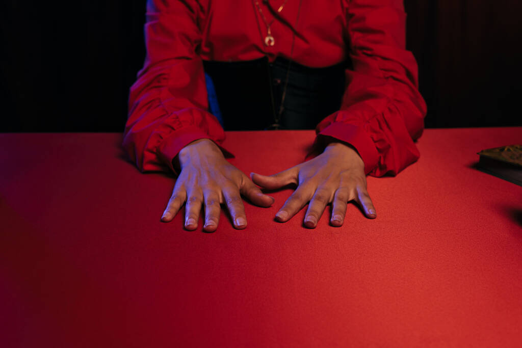 cropped view of medium with hands on red table isolated on black - Foto, Imagem