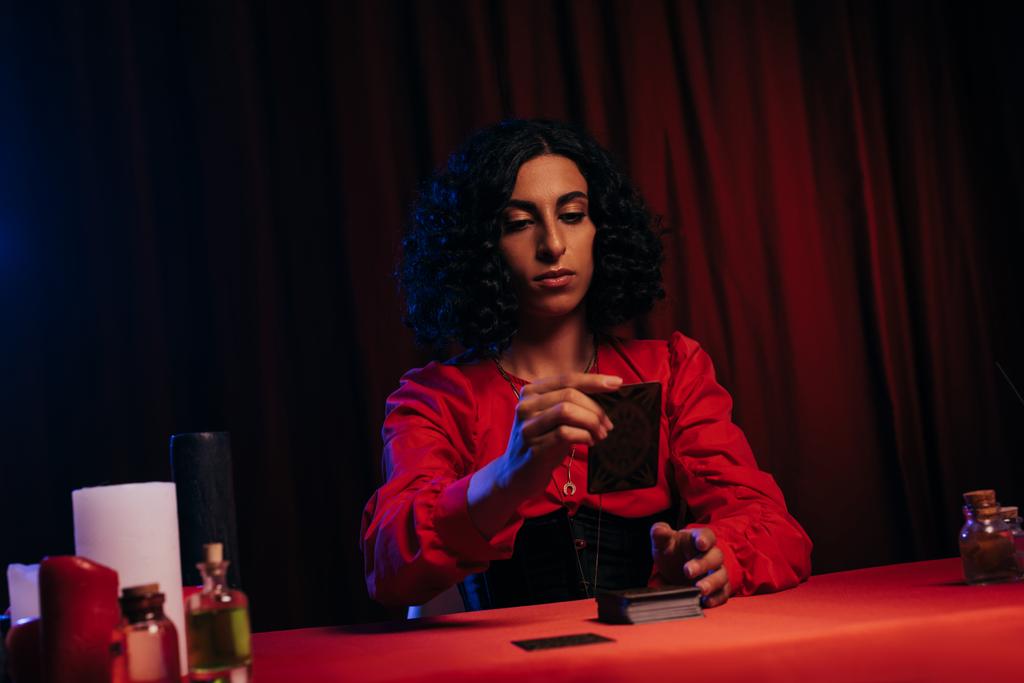 young fortune teller with tarot cards near candles and essential oils on dark background - Foto, Bild
