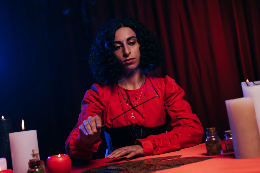 young fortune teller holding palo santo stick near tarot cards on dark background - Photo, Image