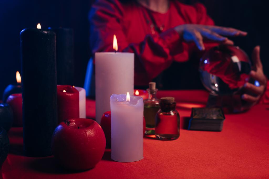 selective focus of blurred candles near cropped fortune teller and crystal ball isolated on black - Zdjęcie, obraz