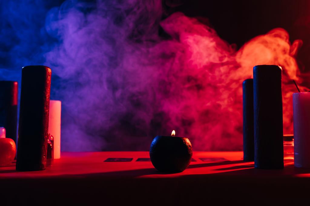 candles and tarot cards near colorful smoke on black background - Valokuva, kuva